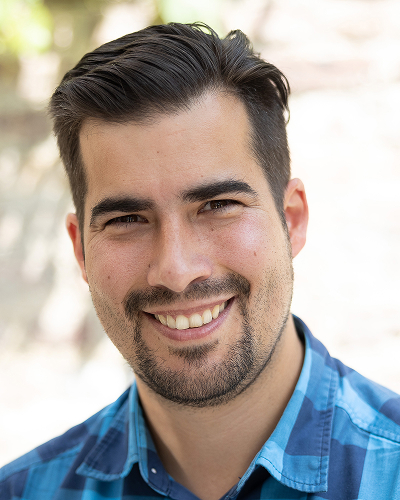 Man in blue checked shirt against a light background smiles into the camera