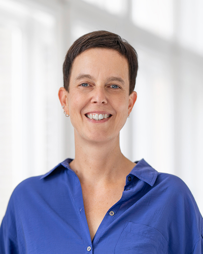Woman in blue blouse against a light background smiles into the camera